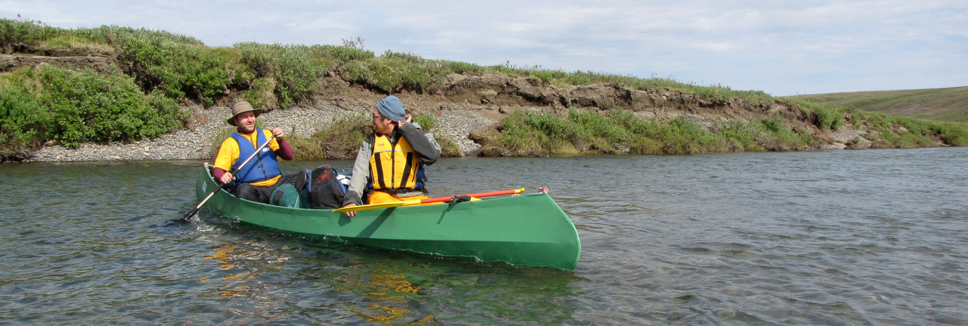2 paddlers discuss the river while steering a canoe in the arctic