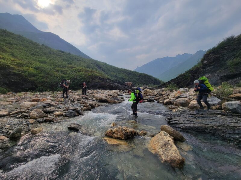 Hikers cross a creek in Gates of the Arctic National Park Alaska on a guided backpacking trip with Arctic Wild